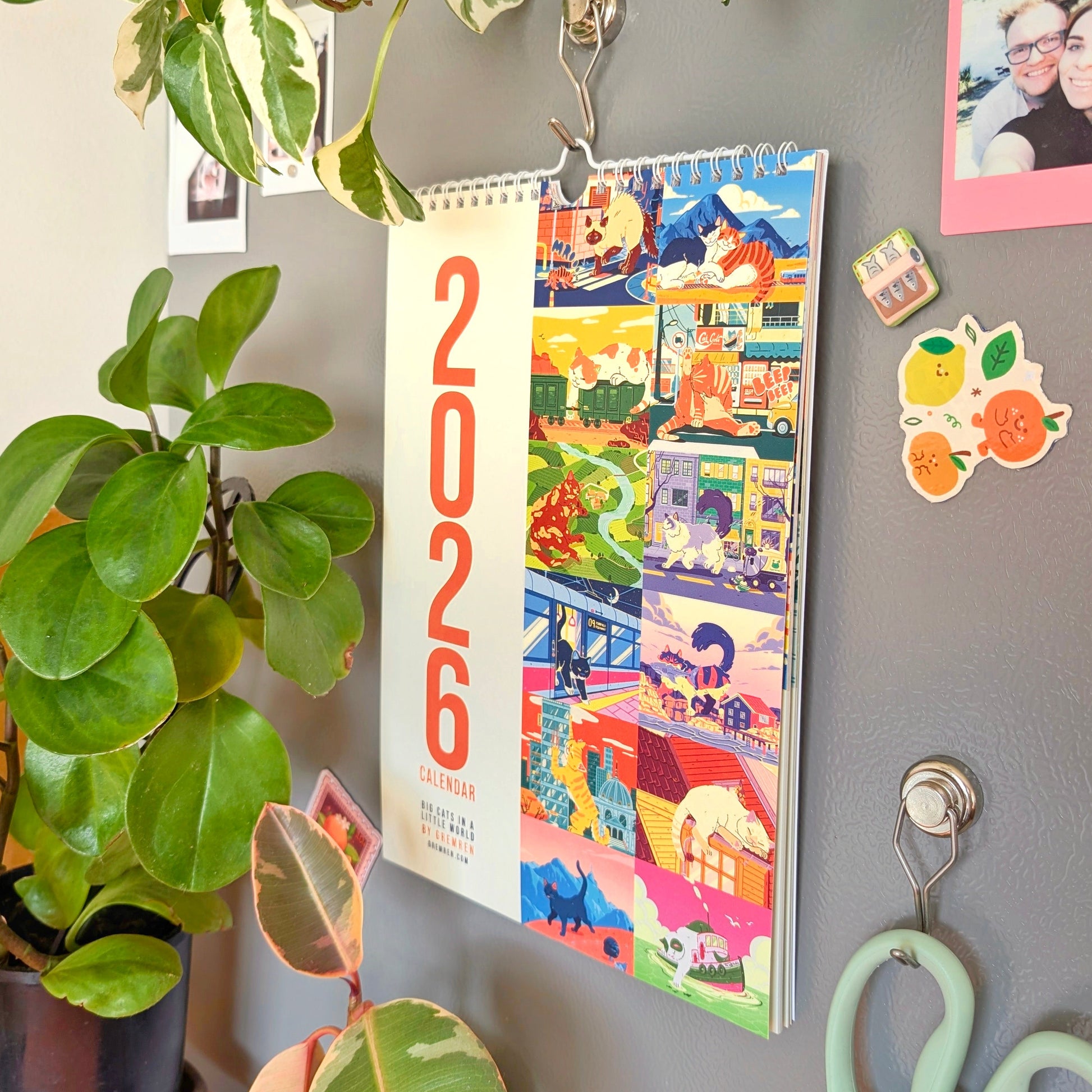 Colorful 2026 calendar on the side of a grey fridge with plants and photos.